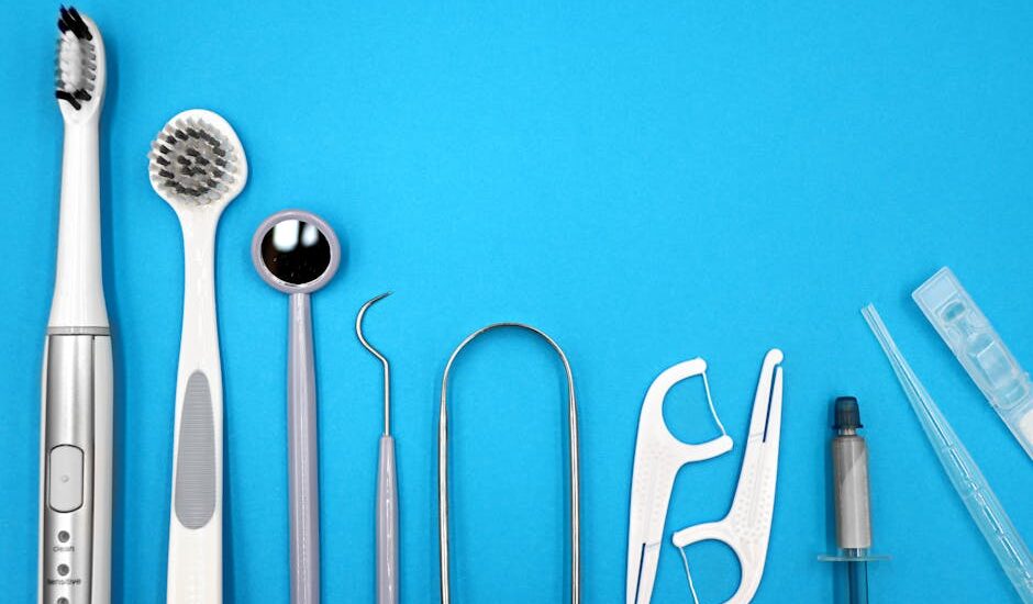water flosser vs dental pick — Flat lay of dental care tools including toothbrushes, dental mirror, and floss sticks on blue background.
