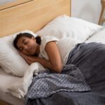 A woman peacefully sleeping in bed using a cozy weighted blanket, promoting relaxation.