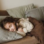 Young child sleeping under a brown blanket on a bed, illustrating considerations for parents choosing weighted blankets for kids.