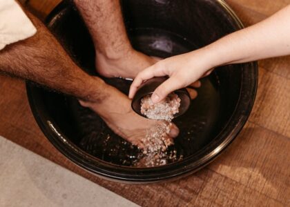 Person soaking feet in a black basin while another hand pours salt crystals, illustrating foot care methods related to foot pads.