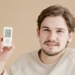 A smiling man holds a glucometer against a beige background, highlighting health awareness.