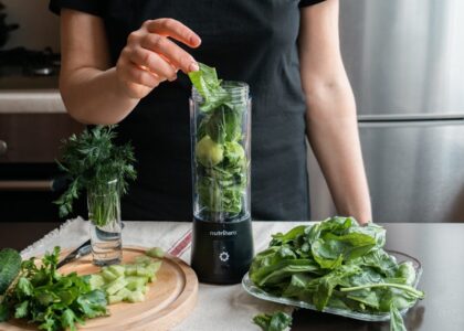 Person preparing a fresh green smoothie with spinach, cucumber, and herbs using a blender.