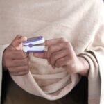 Adult hands measuring oxygen levels using a pulse oximeter, wrapped in a blanket indoors.