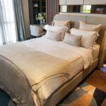 A neatly made bed in a contemporary bedroom with an air purifier positioned beside the nightstand, illustrating bedroom placement tips.