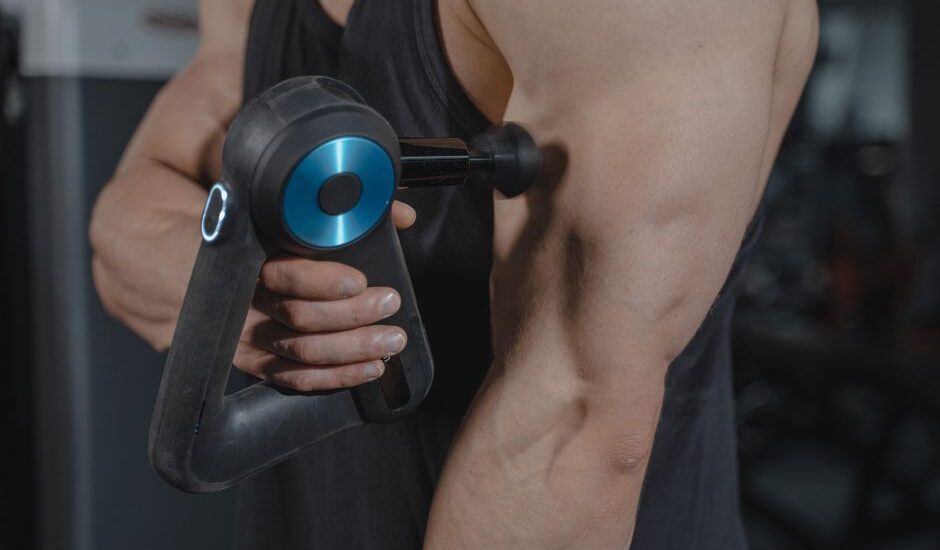 A person using a percussive therapy device on their arm, illustrating benefits of percussive therapy.
