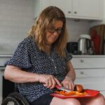 A woman using adaptive utensils to cut food on a red plate, illustrating adaptive eating tools for adults.