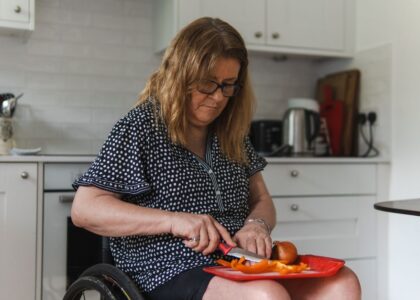 A woman using adaptive utensils to cut food on a red plate, illustrating adaptive eating tools for adults.