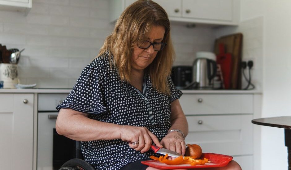 A woman using adaptive utensils to cut food on a red plate, illustrating adaptive eating tools for adults.