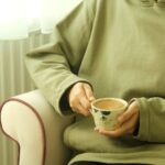 A person holding a cup of coffee while seated next to a leg massager, illustrating relaxation.