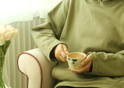 A person holding a cup of coffee while seated next to a leg massager, illustrating relaxation.