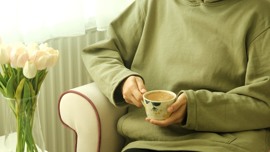 A person holding a cup of coffee while seated next to a leg massager, illustrating relaxation.