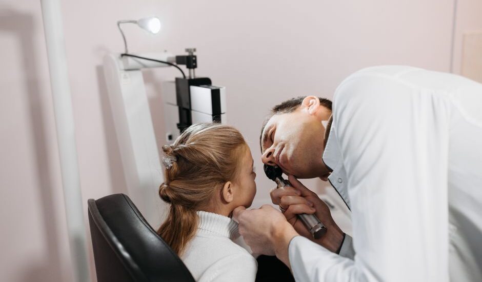 A doctor examines a child's ear, relating to hearing aids and cochlear implants.