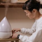 A person adjusting a humidifier, illustrating the function of humidifiers in contrast to dehumidifiers.