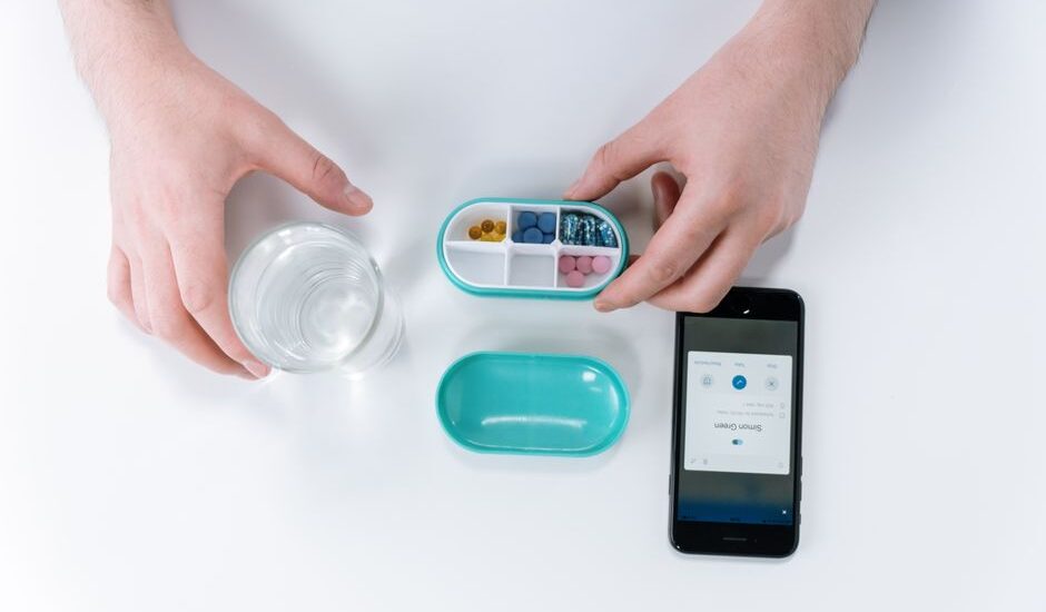 A person using an electronic medication dispenser with a smartphone app and a glass of water.