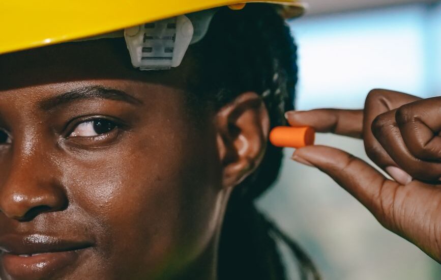 A person holding an orange foam earplug near their ear, illustrating foam earplugs vs silicone earplugs.