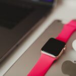 A fitness tracker with a pink band is placed next to a laptop and earbuds, illustrating how to charge a fitness tracker.