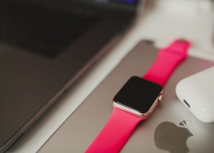 A fitness tracker with a pink band is placed next to a laptop and earbuds, illustrating how to charge a fitness tracker.