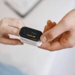 A person demonstrates how to disinfect a pulse oximeter while holding it.
