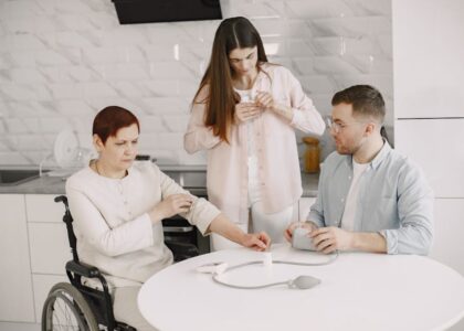 A woman in a wheelchair receives assistance with a portable oxygen concentrator refill in a kitchen.