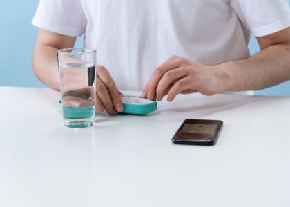 A person demonstrates a pill splitter while holding a pill and glass of water, related to pill splitter reviews.