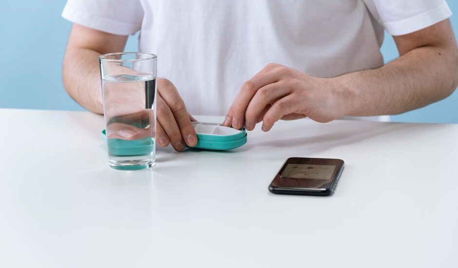 A person demonstrates a pill splitter while holding a pill and glass of water, related to pill splitter reviews.