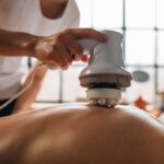 A person using a pulse massager on someone's back for pain relief.
