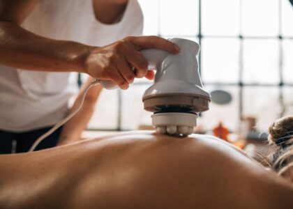 A person using a pulse massager on someone's back for pain relief.