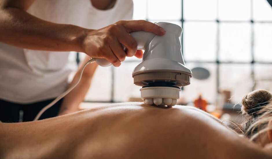A person using a pulse massager on someone's back for pain relief.