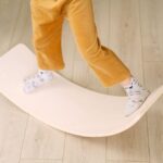 A child stands on a wooden balance board, showcasing its use in exercise.