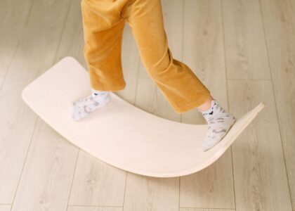 A child stands on a wooden balance board, showcasing its use in exercise.