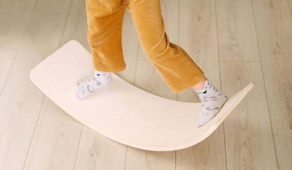 A child stands on a wooden balance board, showcasing its use in exercise.