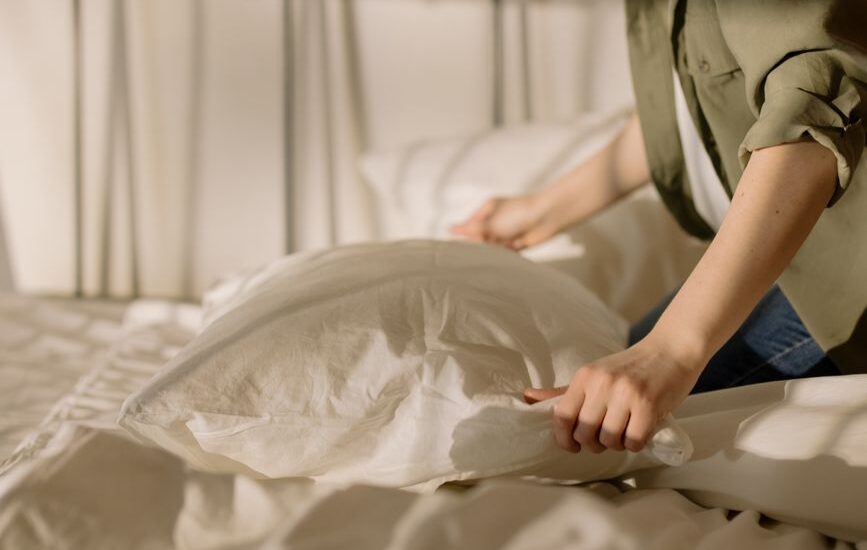 A person adjusting a white orthopedic pillow on a bed, illustrating cleaning techniques.