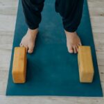 A person stands on a yoga mat with wooden blocks, illustrating how to disinfect yoga blocks.