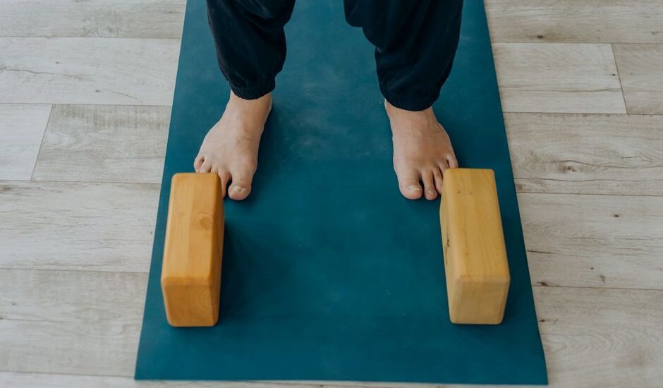 A person stands on a yoga mat with wooden blocks, illustrating how to disinfect yoga blocks.