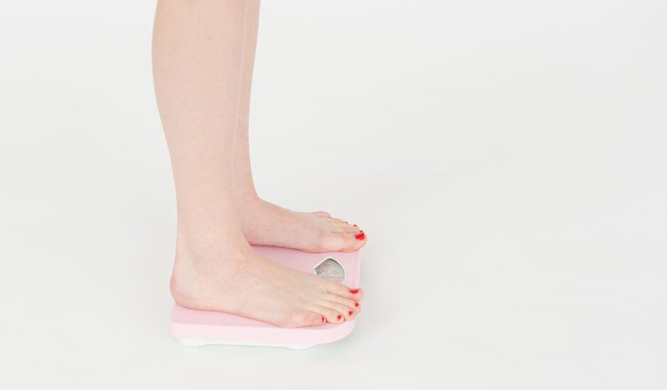 A person stands on a smart bathroom scale, illustrating its use with iPhone syncing.