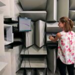 A woman operates a digital force gauge in a soundproof testing room, illustrating its use.