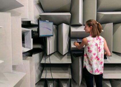 A woman operates a digital force gauge in a soundproof testing room, illustrating its use.
