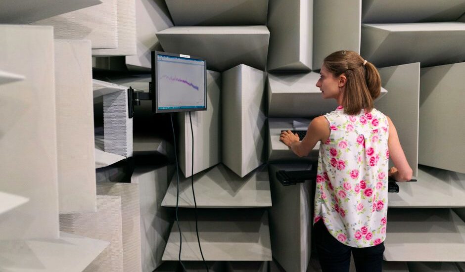 A woman operates a digital force gauge in a soundproof testing room, illustrating its use.